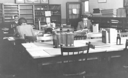 Black and white photo of students studying in group reading room.